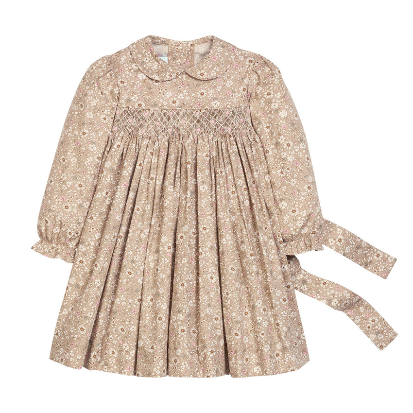 A long-sleeve children's dress in a beige and brown floral print, featuring a smocked bodice, Peter Pan collar, and a tie belt on the side, shown against a plain white background.