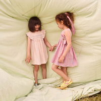 Two young girls in pink dresses standing on a large green backdrop.
