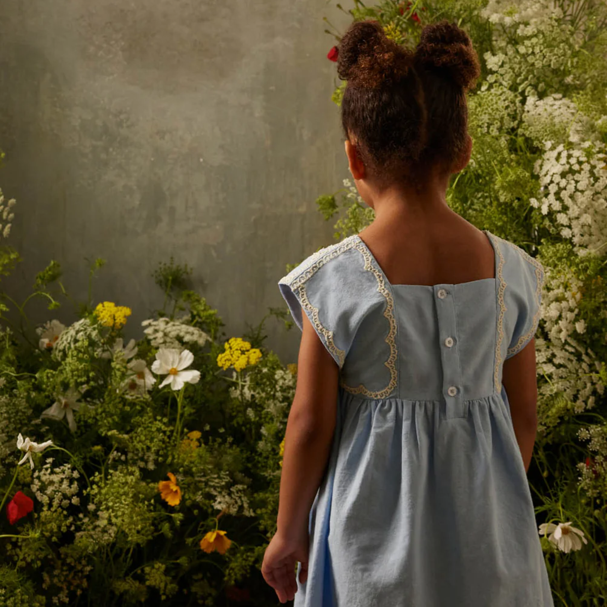 Blue dress with white trim and back buttons in a garden setting.