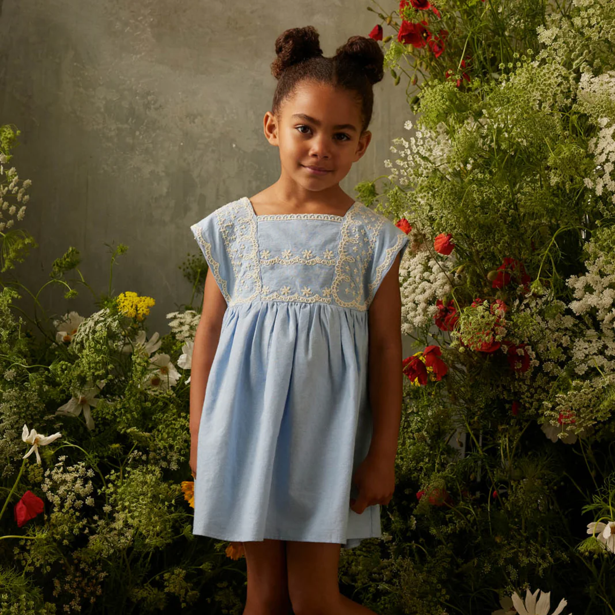 Young girl in a blue dress with white trim in a garden setting.