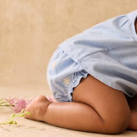 Baby wearing a light blue diaper cover with floral patterns on a beige background.