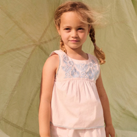 Young girl wearing a pink top with floral embroidery against a green background.