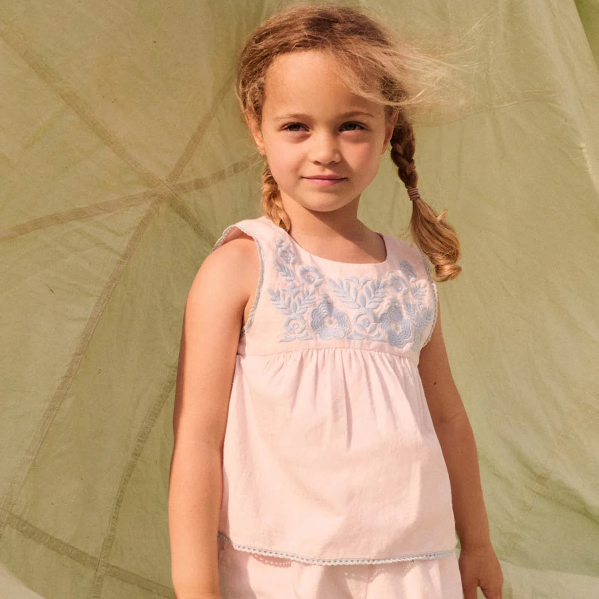 Young girl wearing a pink top with floral embroidery against a green background.