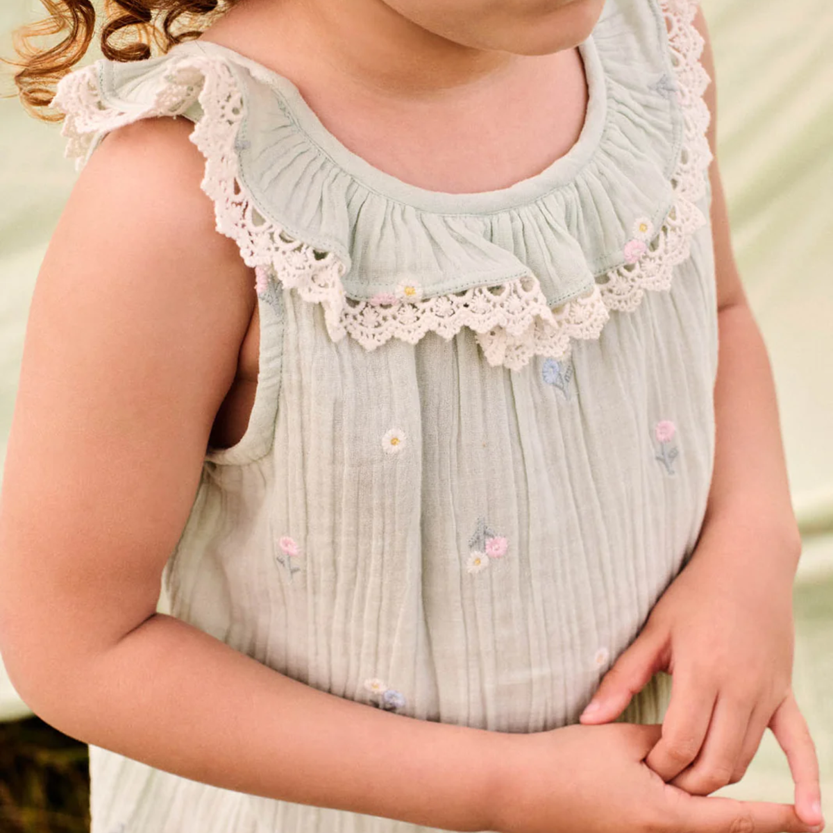 Light blue sleeveless top with lace trim collar and floral embroidery on a blurred background.