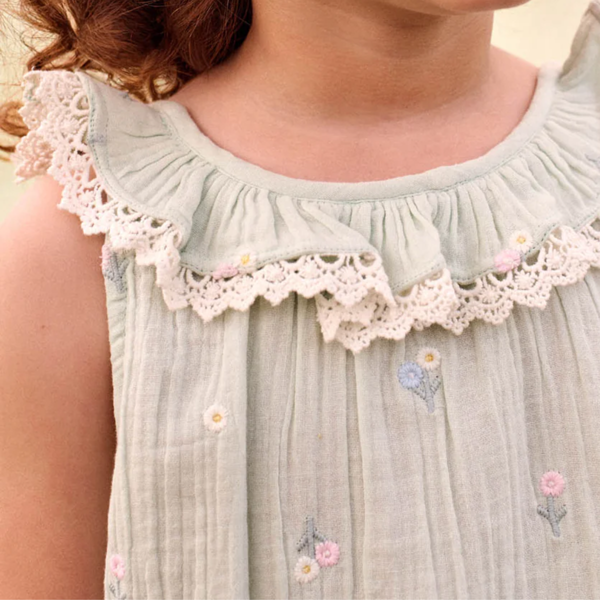 Light green blouse with lace trim and floral embroidery on a blurred background.