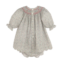 A girl's smocked dress with short puff sleeves, a scalloped hem, and a tiny floral print on a light gray background with pink and green details. It features a smocked neckline with pink embroidered trim and decorative buttons down the back.