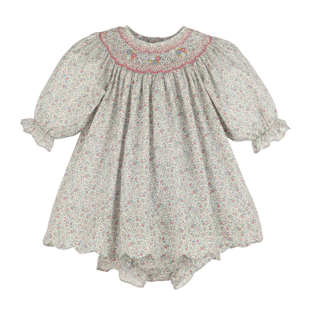 A girl's smocked dress featuring a delicate multicolor floral print on a light grayish-beige background, with a pink embroidered neckline and ruffled sleeves.