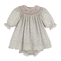 A girl's smocked dress featuring a delicate multicolor floral print on a light grayish-beige background, with a pink embroidered neckline and ruffled sleeves.