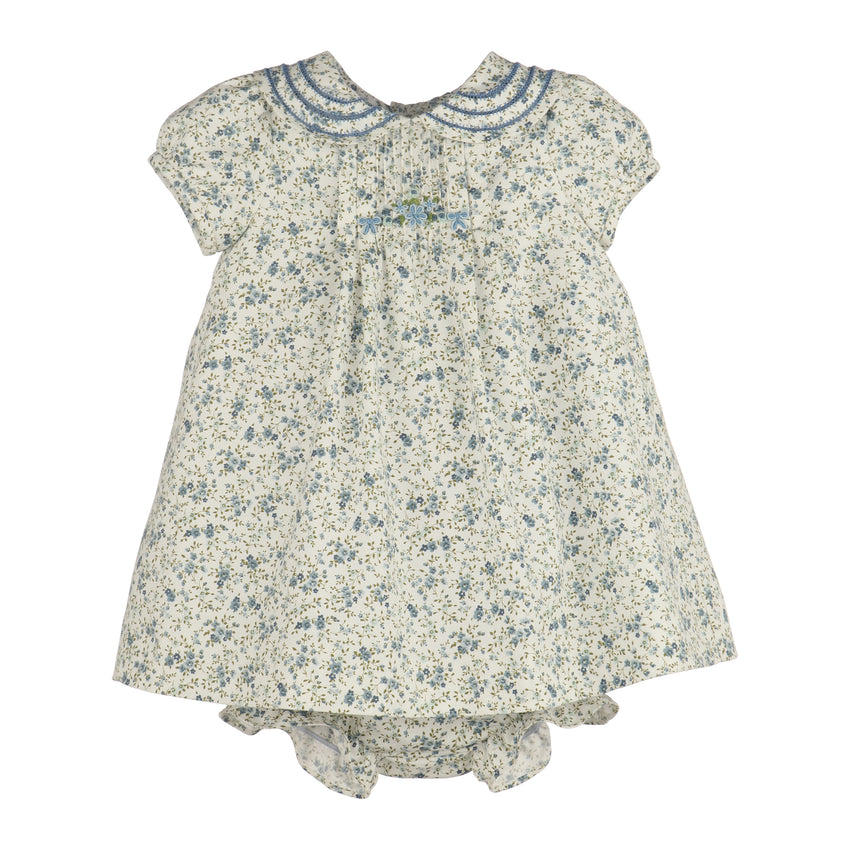 A girl's short-sleeve dress and matching bloomers set in a cream-colored fabric with a blue and green floral print. The dress features a Peter Pan collar with blue embroidered trim and a small blue bow at the center chest.