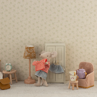 Stuffed mouse toy trying on clothes  in a room with a lamp, chair, and small table.