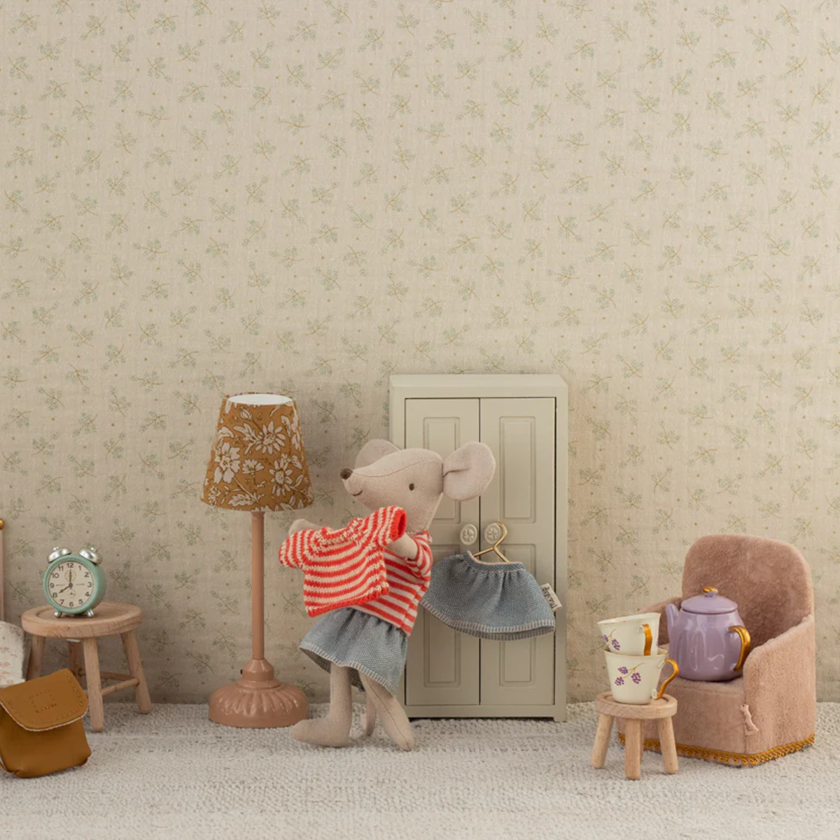 Stuffed mouse toy trying on clothes  in a room with a lamp, chair, and small table.