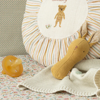 Yellow bunny rattle on a bed with a pillow, pacifier and blanket.
