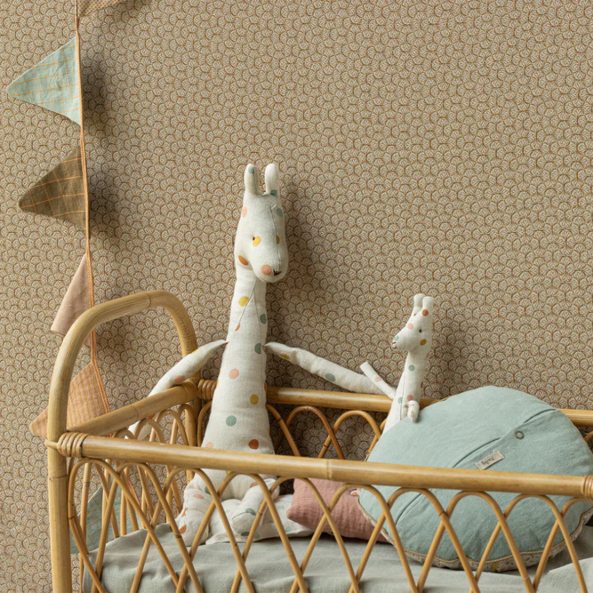 Two polka dot giraffes in a bamboo baby bed with a pillow and flags.
