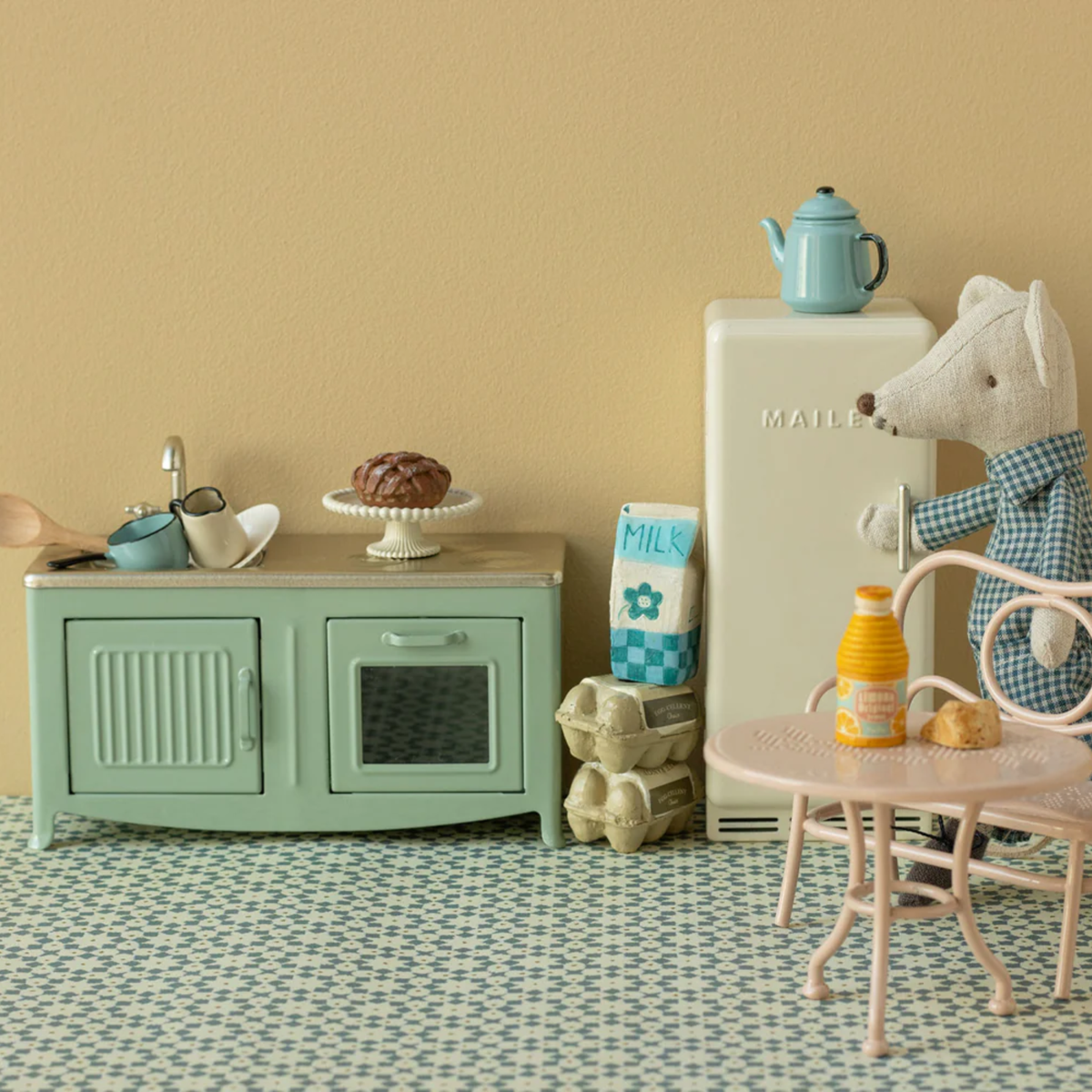 Mouse in its kitchen with table, refrigerator, sink, oven, eggs, coffee pot and a small table and chair.