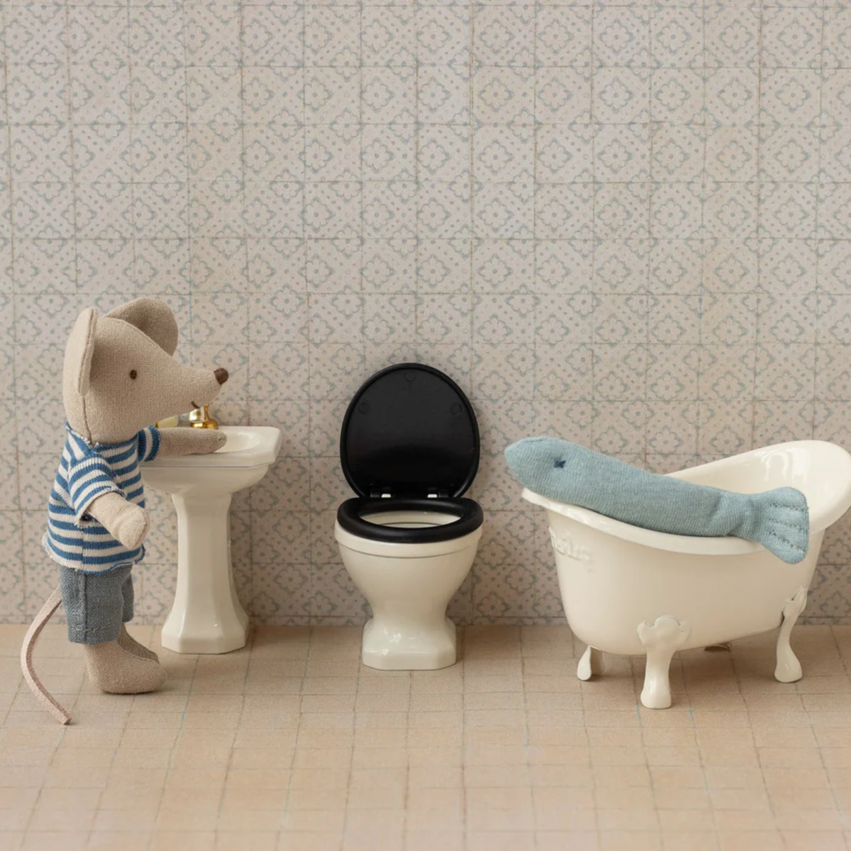 Miniature bathroom set with toy mouse, sink, toilet, and bathtub against a patterned wall.  Fish in bathtub.