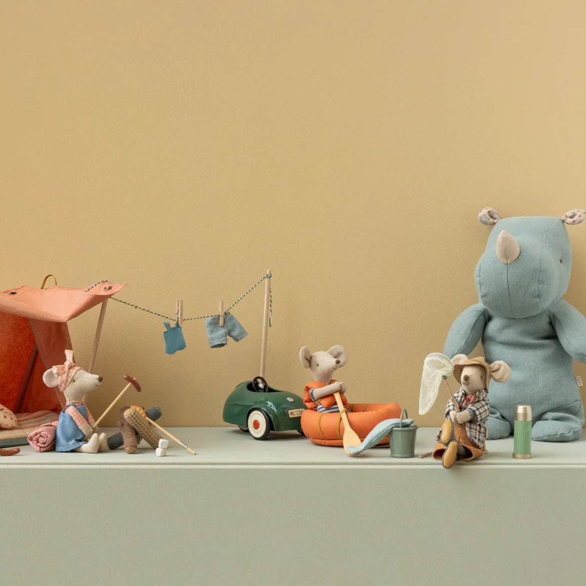 Set of toy mice at a 'campsite' with a rhino  and camp items on a shelf against a beige wall.