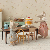 Two royal mice in a kitchen with a cake in a room with floral wallpaper.