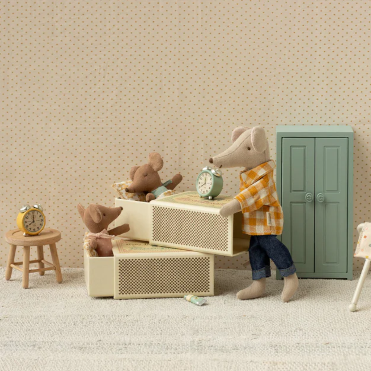 Toy mice in their matchbox beds, a dad mouse overseeing them  Clocks and dresser in room against a beige wall.
