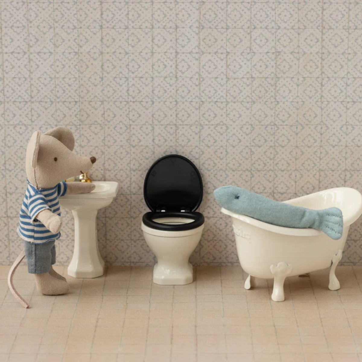 Miniature bathroom set with a mouse character, toilet, and bathtub against a patterned wall.