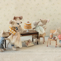 Stuffed toy mice family gathered around a table with a cake, set against a floral wallpaper background.