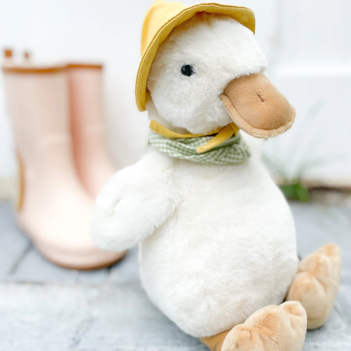 Plush duck toy wearing a yellow hat and green scarf on a light background.