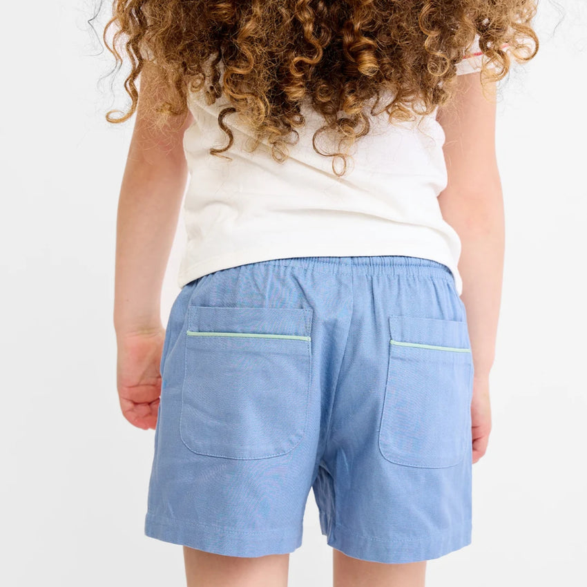 Back view of a child wearing light blue shorts with two back pockets and a white sleeveless top, shown against a plain white background.