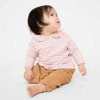 A baby sitting on a white studio background, wearing a pink and white striped long-sleeve top with a ruffled collar and tan pants.