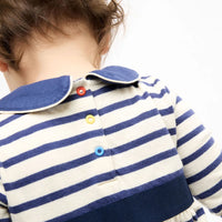 Close-up back view of a child wearing a cream and navy blue horizontally striped long-sleeve top with a blue collar and colorful snap buttons.