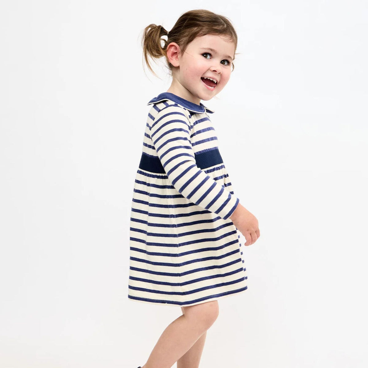 A young child wearing a navy blue and white horizontally striped long-sleeve dress, photographed against a clean white studio background.
