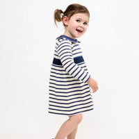 A young child wearing a navy blue and white horizontally striped long-sleeve dress, photographed against a clean white studio background.