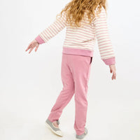 A child shown from the back wearing a pink and white striped long-sleeve top with solid pink ribbed cuffs and hem, paired with pink sweatpants and white shoes, against a plain white studio background.