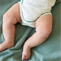 Close-up of a baby's legs wearing a white bodysuit with green trim, sitting on a textured green blanket.