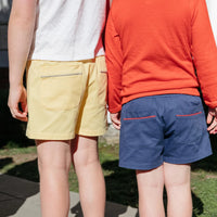 Two kids wearing shorts, one yellow and one blue, standing outdoors.