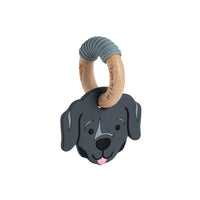A dog-shaped baby teething toy featuring a dark gray silicone dog head with a pink tongue and a natural wood ring handle wrapped in a gray ribbed sleeve, shown on a plain white background.
