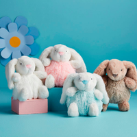 Four plush bunny toys in different colors on a blue background with a large flower decoration.