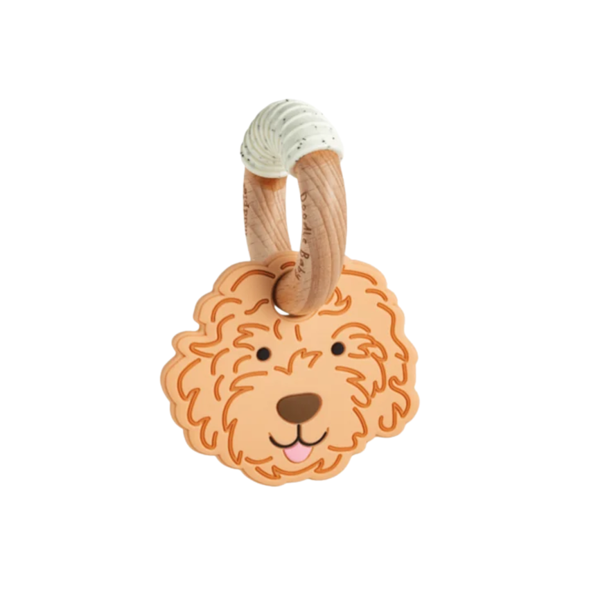 A baby teething toy featuring a sculpted golden doodle dog face in a warm terracotta-brown color, attached to a natural wood ring with a beige ribbed silicone loop at the top, shown on a plain white background.