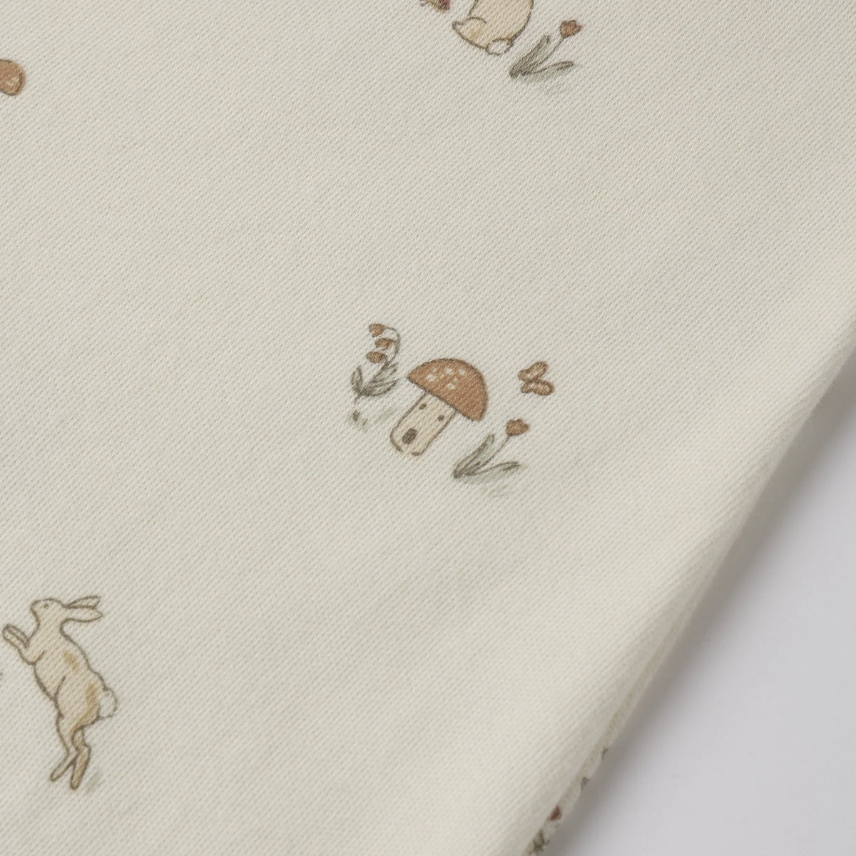 A close-up of cream-colored fabric printed with small whimsical illustrations of rabbits, mushrooms, and flowers in muted brown and tan tones.
