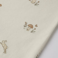 A close-up of cream-colored fabric printed with small whimsical illustrations of rabbits, mushrooms, and flowers in muted brown and tan tones.
