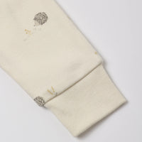 Close-up of a cream-colored knit cuff with a small embroidered hedgehog and gold floral detail on the upper section.