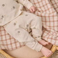 A baby wearing a cream-colored two-piece outfit with small brown and beige hedgehog prints, lying on a brown and white checkered blanket.