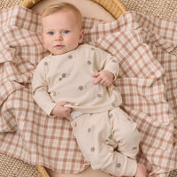 A baby lying on a woven blanket, wearing a cream long-sleeve pajama set with small gray and brown woodland animal prints. 