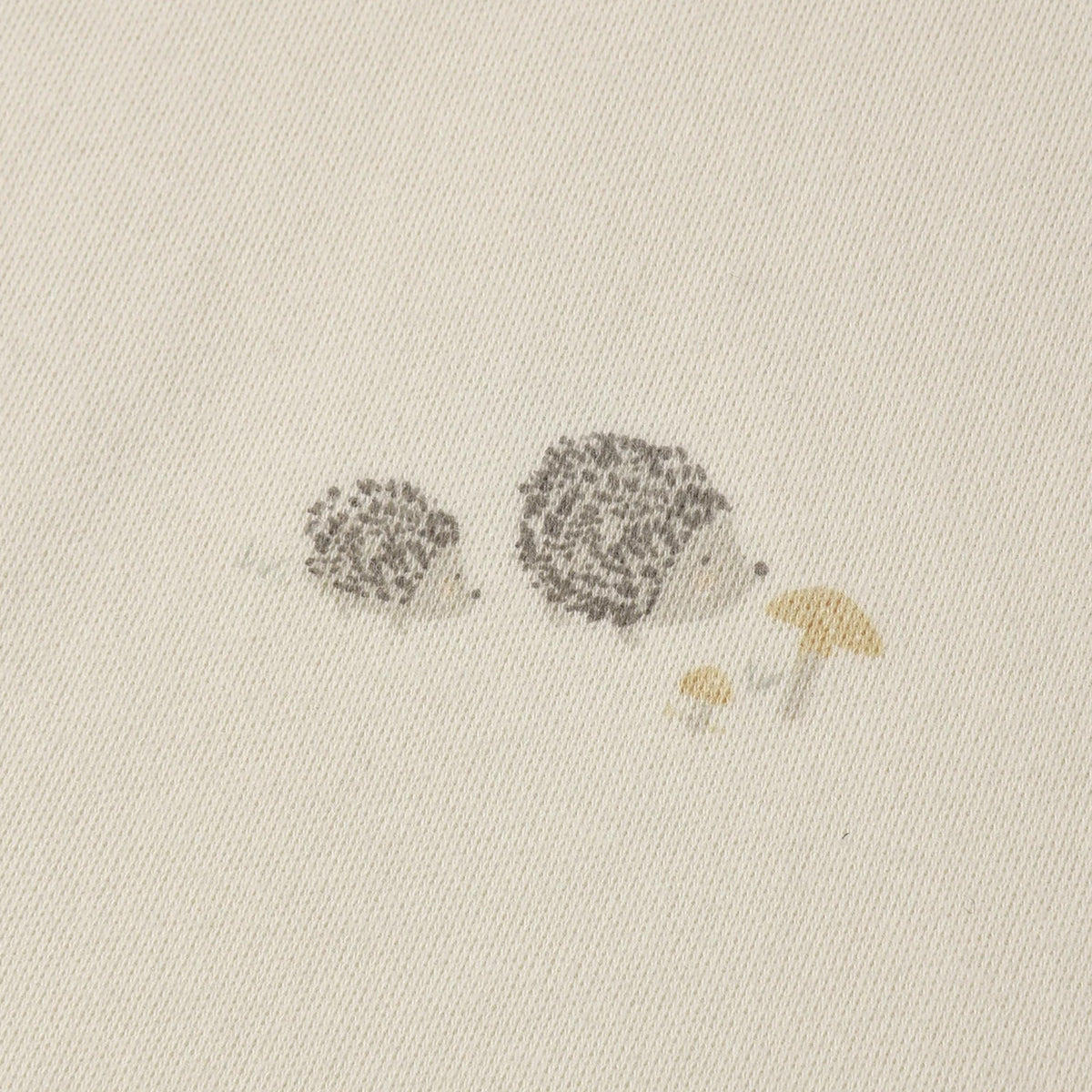 Close-up of a cream-colored fabric with a delicate printed design of two small hedgehogs and two tiny mushrooms in muted gray and mustard yellow.