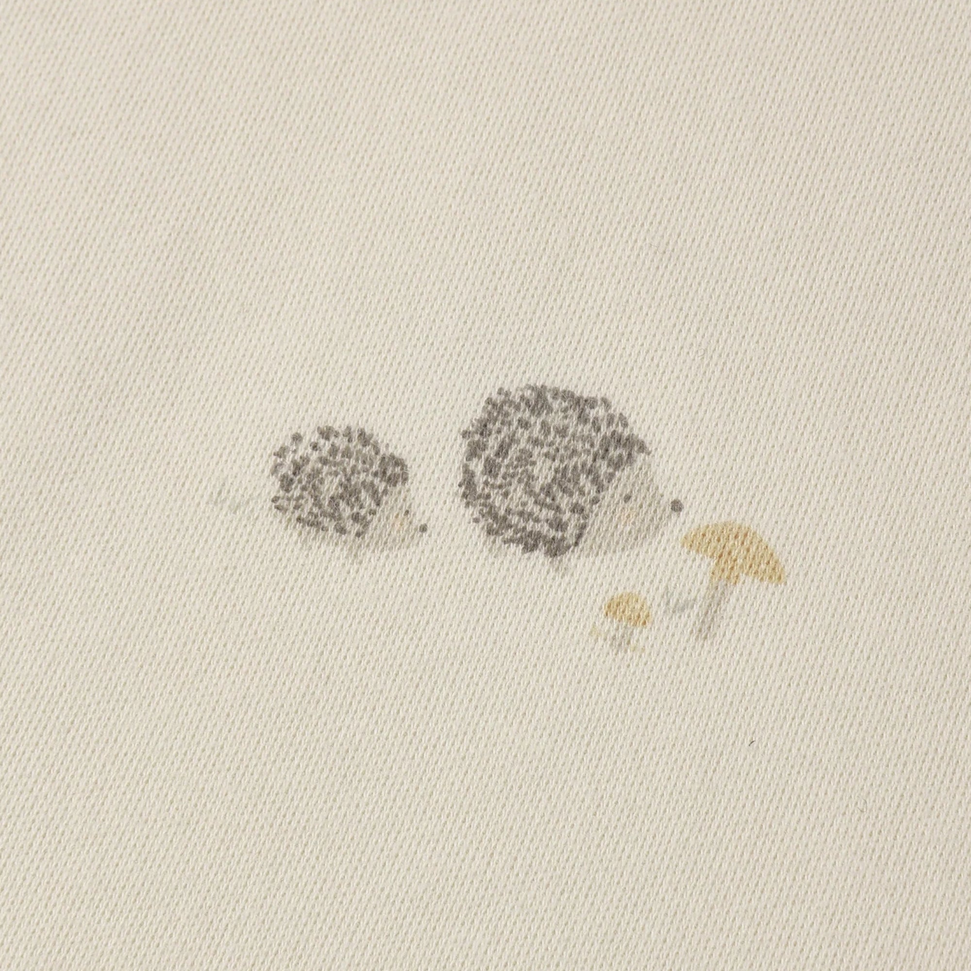 Close-up of a cream-colored fabric with a delicate printed design of two small hedgehogs and two tiny mushrooms in muted gray and mustard yellow.