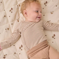 A baby lying on a quilted cream mattress  wearing a beige and white striped long-sleeve wrap bodysuit and tan pants.