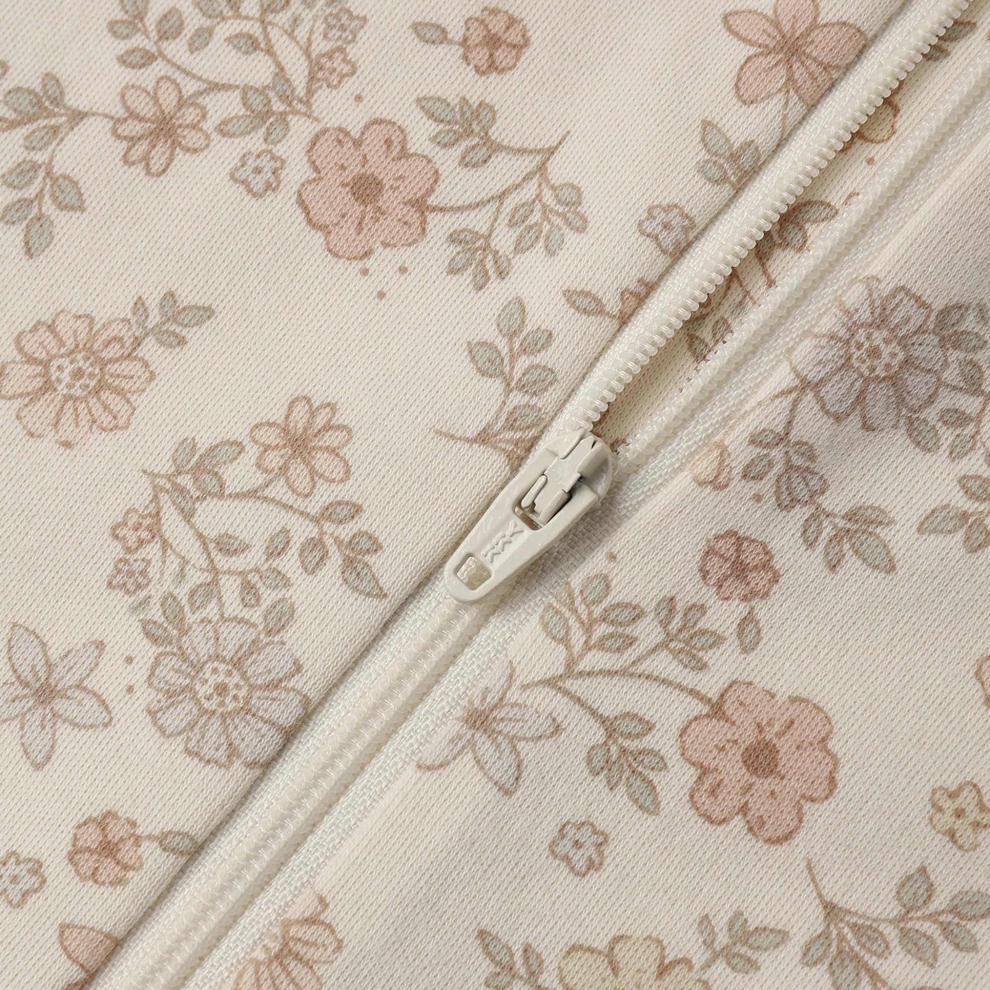 Close-up of a cream-colored zipper from a one-piece floral outfit with pink and beige flowers and muted green leaves.