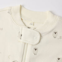 Close-up of a baby sleep suit or onesie in cream/off-white with a small sheep print and a snap-button closure at the neck.