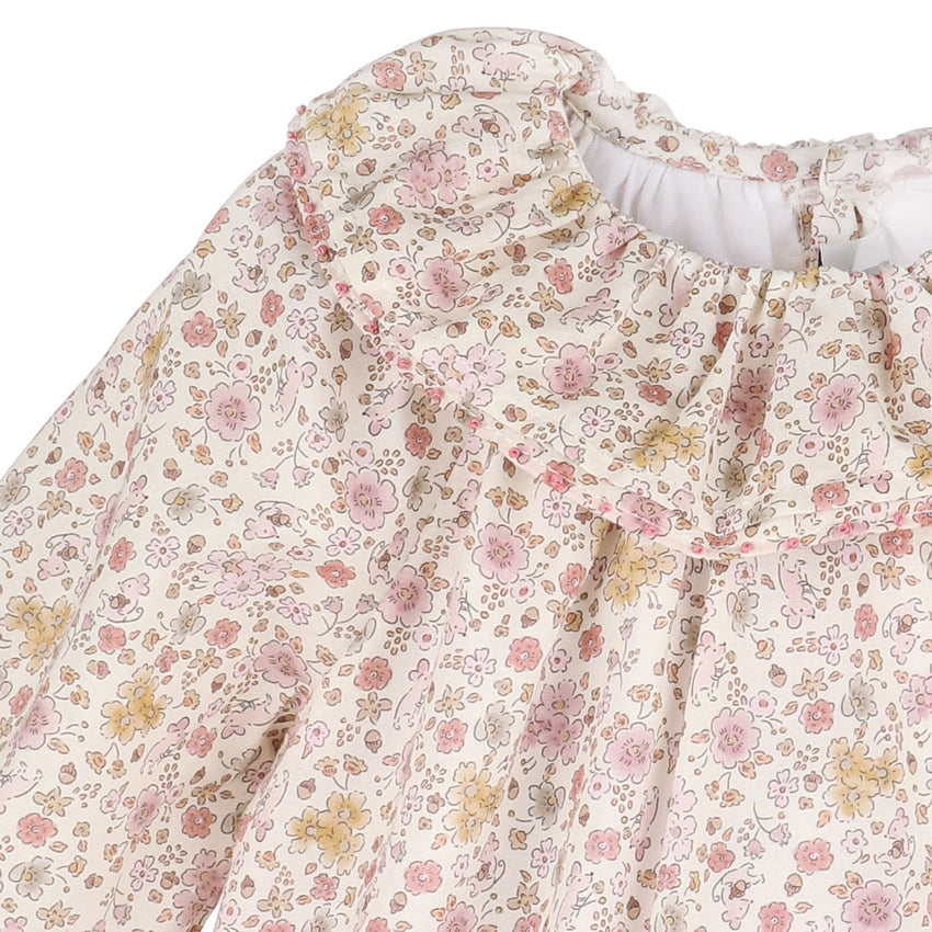 Close up of loral patterned fabric dress with pink, yellow, and green flowers on a white background.