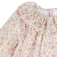 Close up of loral patterned fabric dress with pink, yellow, and green flowers on a white background.