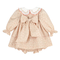 A girl's long-sleeve dress with a small floral print in beige, pink, and green, featuring a large bow at the center back, a white Peter Pan collar with pink trim, and ruffled cuffs and hem.