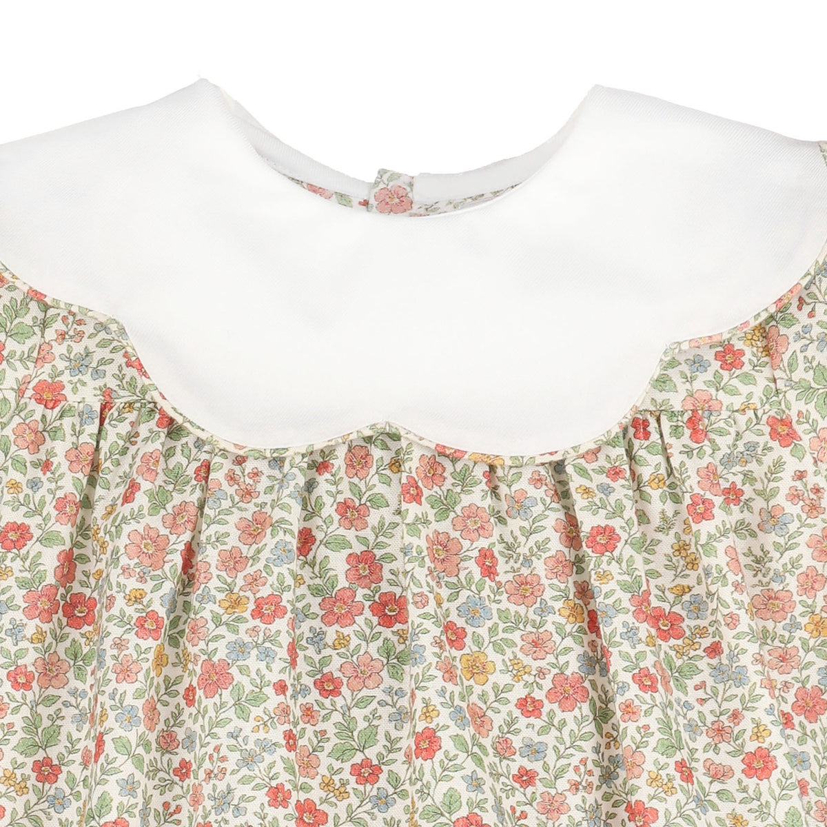 Close-up of a children's dress with a white Peter Pan collar and a cream floral print bodice featuring red, pink, and green flowers.